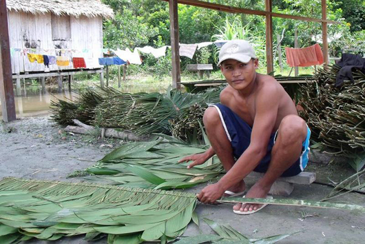Man kneeling on ground with big leaves for thatching